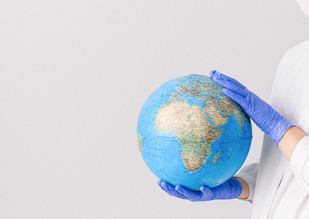 hand in blue gloves holding a globe against a gray background