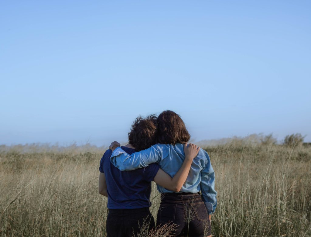 Two people in a field, backs to the camera, and arm around one another