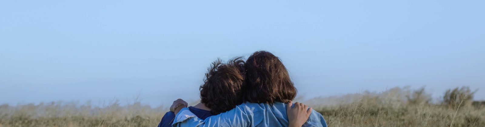 Two people in a field, backs to the camera, and arm around one another