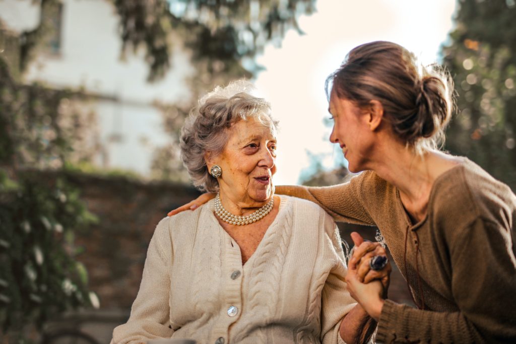 Joyful adult daughter greeting her happy , surprised senior mother in garden