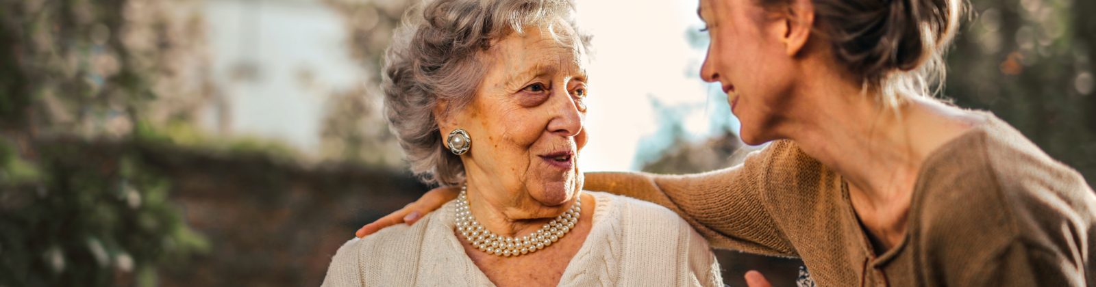 Joyful adult daughter greeting her happy , surprised senior mother in garden