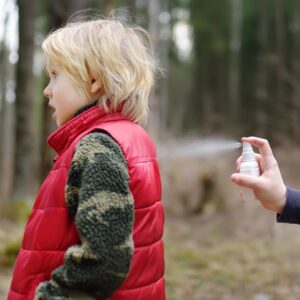 Blond child with just the hand of another person visible spraying their clothes from a white bottle.