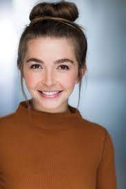 Jake Picker, a white woman with her long blond hair piled on her head, wearing a camel color turtleneck